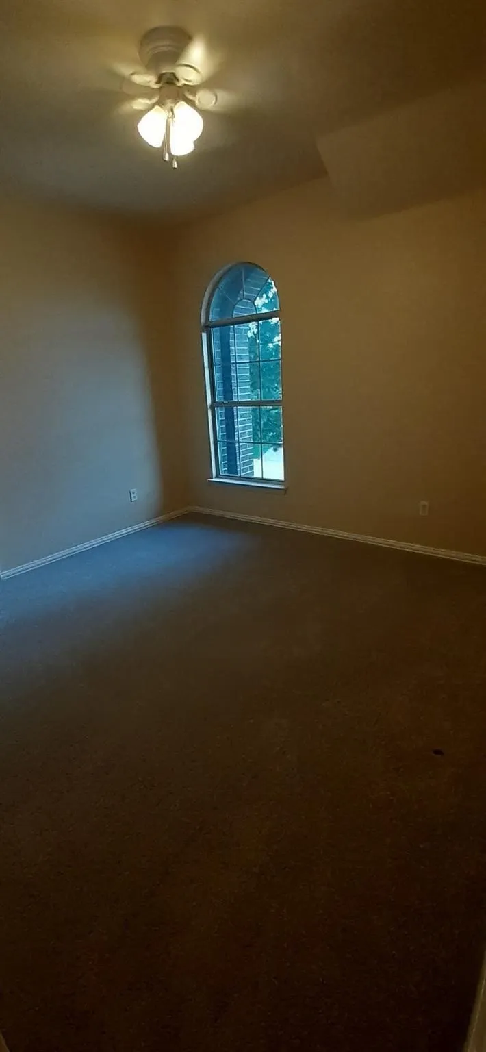 Arched window with exterior light, neutral tone walls, and a ceiling fan with integrated lighting