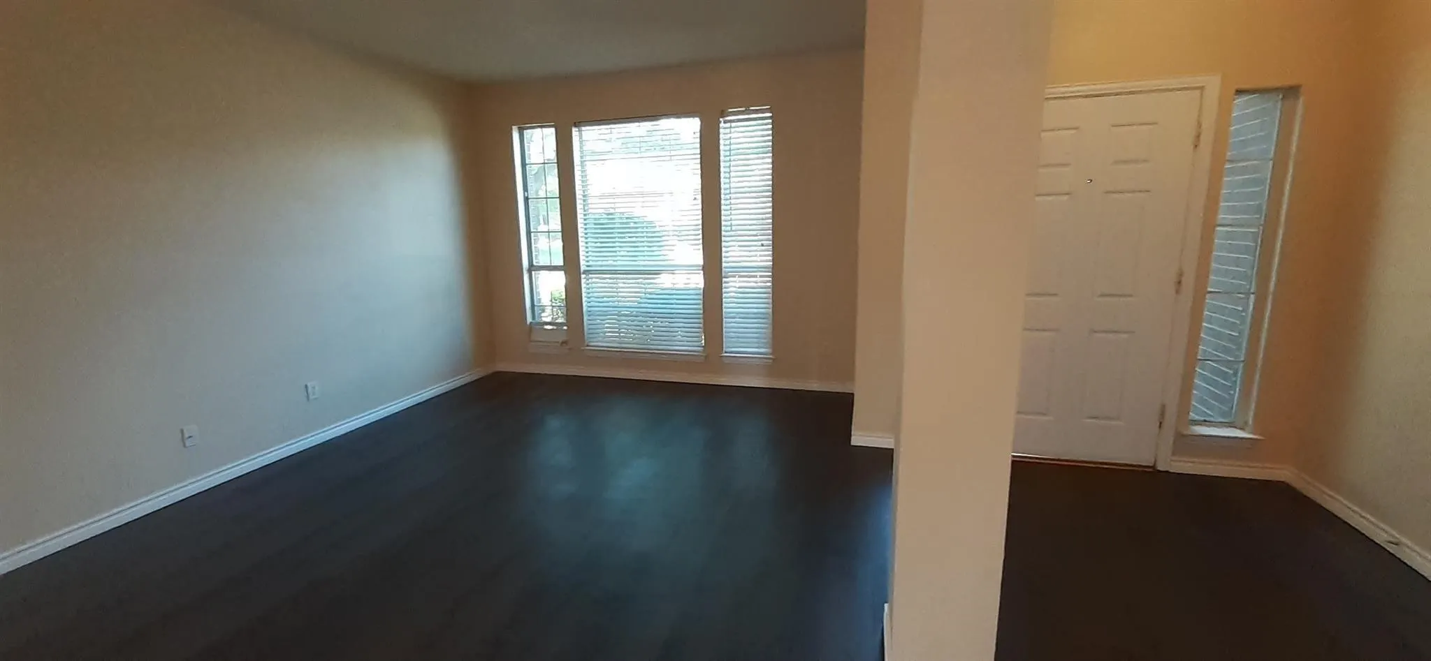 Wood-finish flooring throughout, large windows with horizontal blinds, and a paneled entry door with a sidelight window