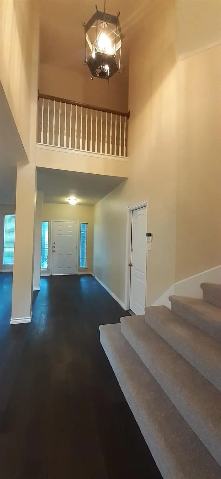 Two-story foyer with a decorative chandelier, wood-finish flooring, and a carpeted staircase with a white spindle railing