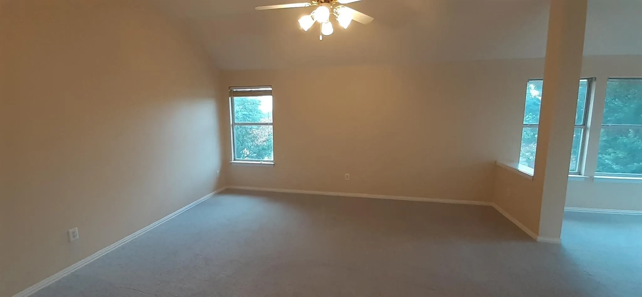 Vaulted ceiling with an attached ceiling fan and light fixture, multiple windows, and light-colored carpeting