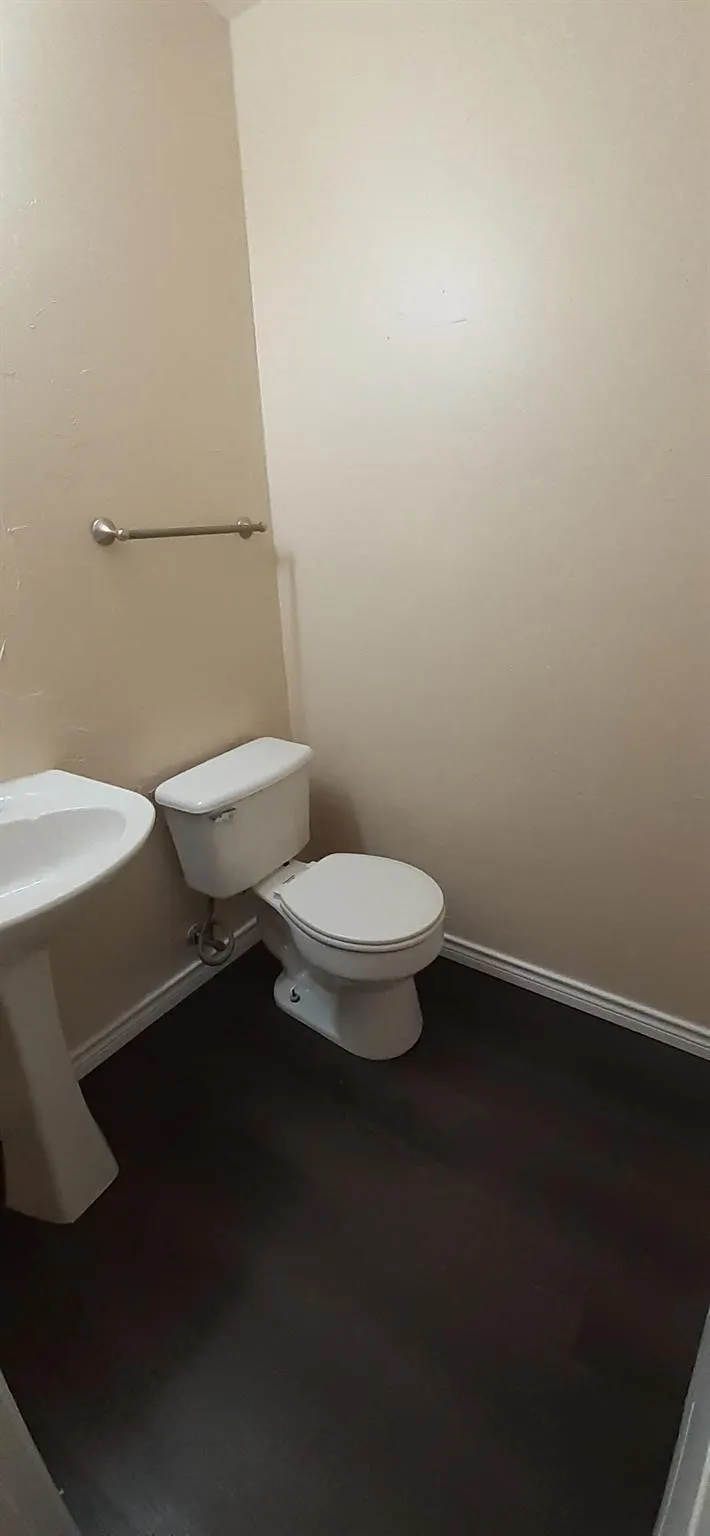 Pedestal sink, toilet, dark wood-finish flooring, and a wall-mounted towel bar