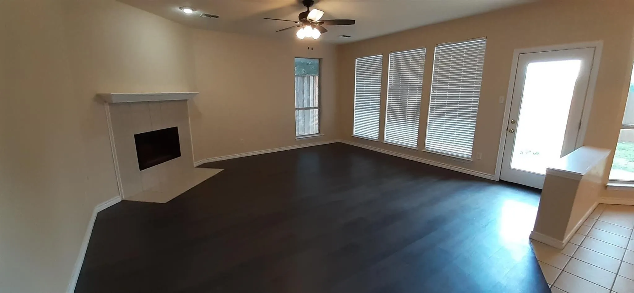 Spacious living area featuring dark wood-finish flooring, a corner fireplace with a tiled surround, recessed lighting, and a ceiling fan