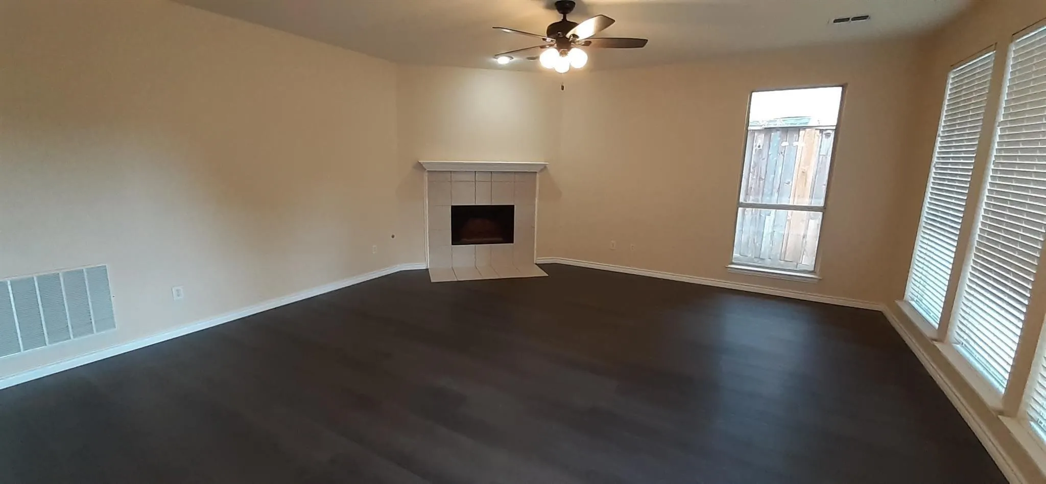 Spacious interior with dark wood-finish flooring, a tiled fireplace, and multiple windows with blinds