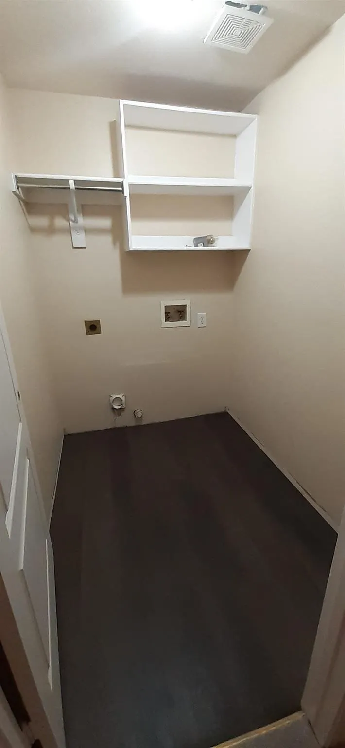 Laundry area featuring built-in shelving, a clothes hanging rod, and dark wood-finish flooring