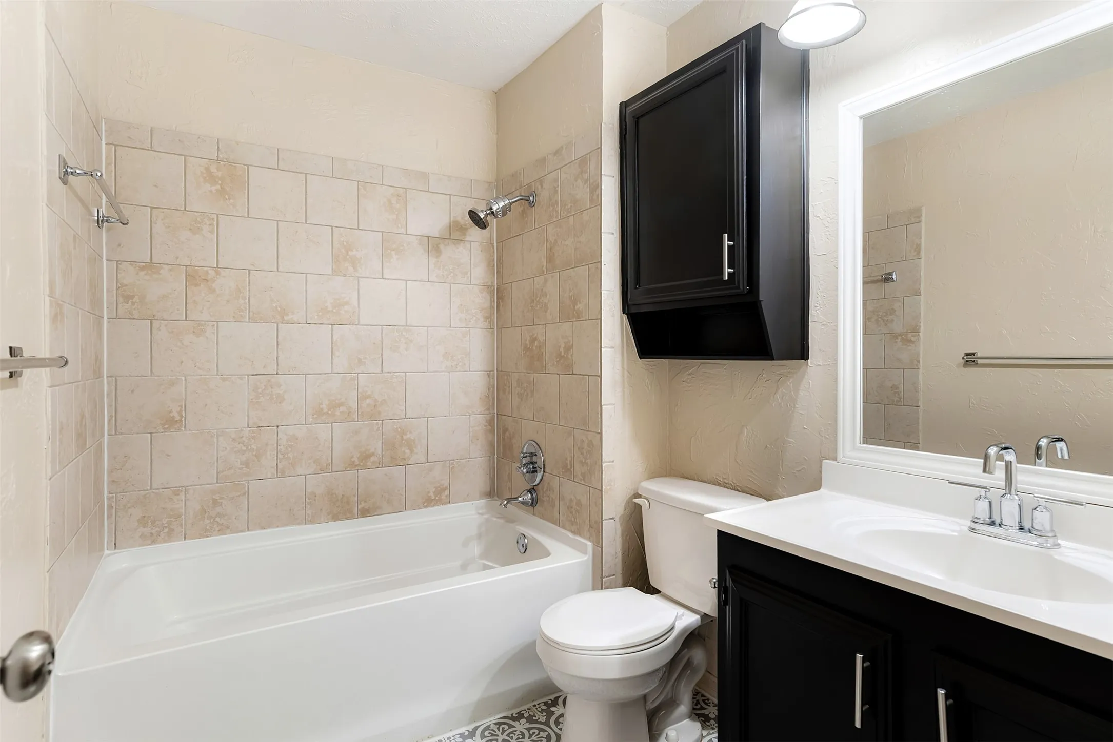 Bathroom featuring a white bathtub, ceramic tile shower surround, dark wood-finish vanity with an integrated sink, wall-mounted mirror, and patterned floor tile