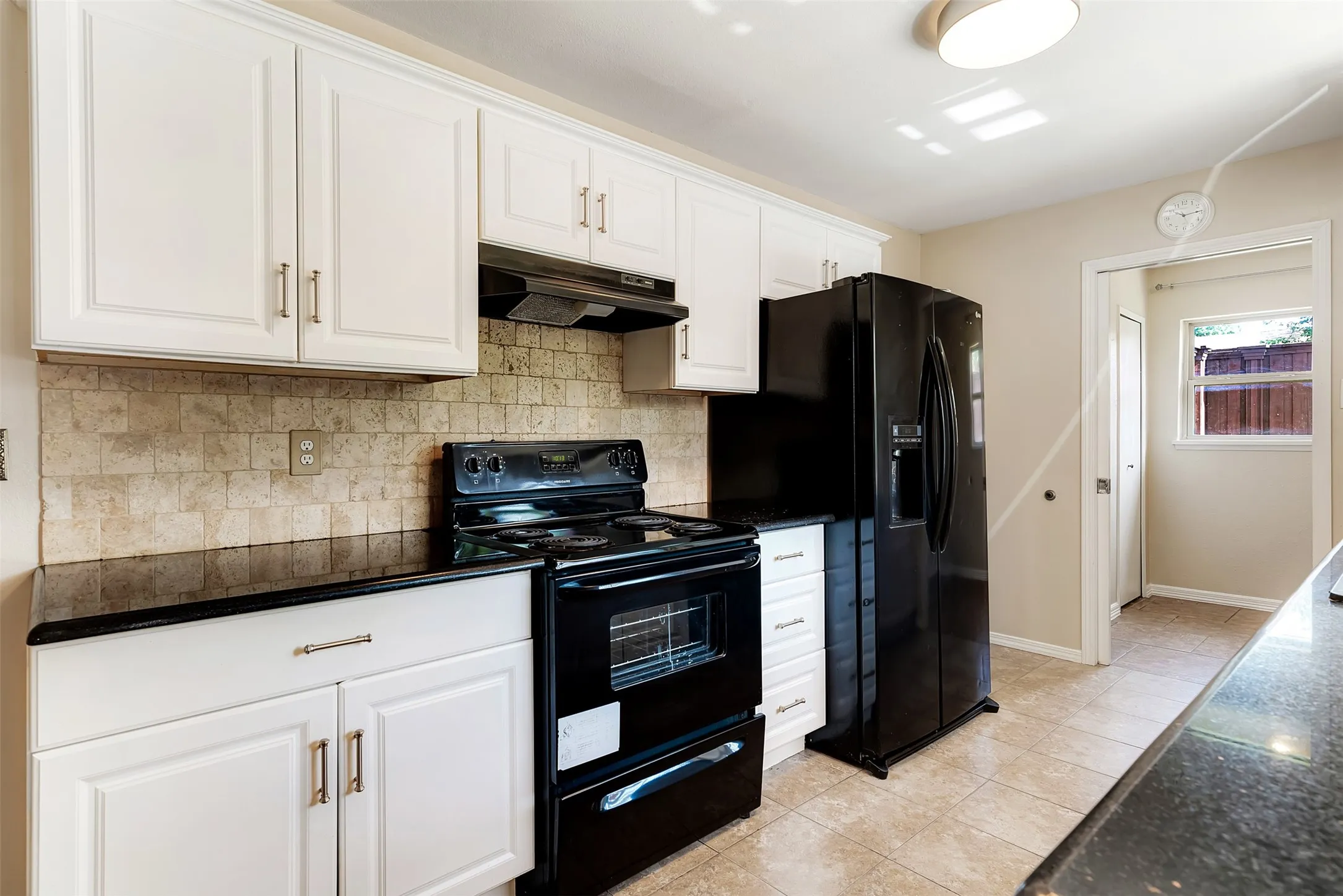 White cabinetry with brushed nickel hardware, black countertops, tile backsplash, black range, and side-by-side refrigerator