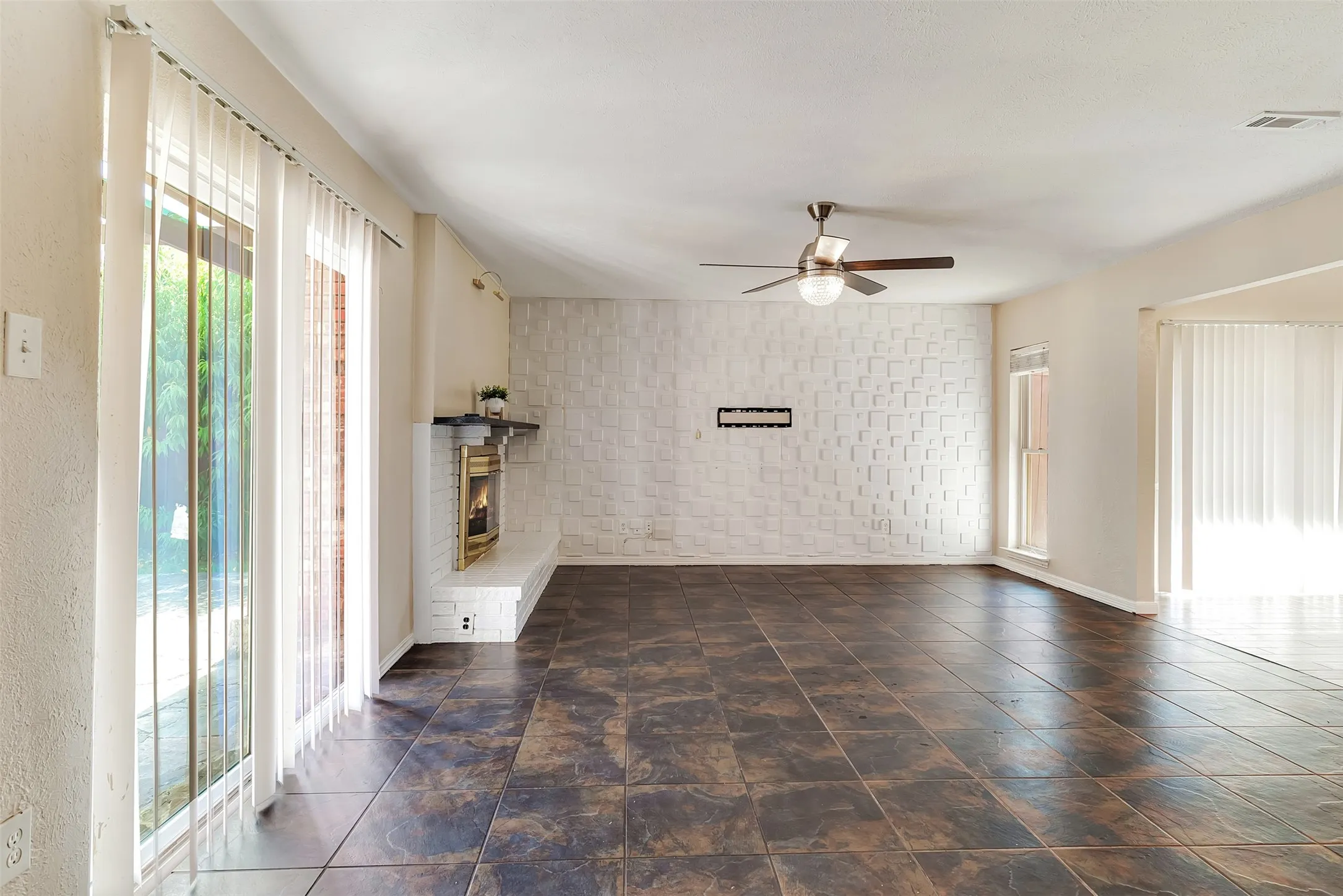 Tiled flooring, brick fireplace with mantel, ceiling fan, and sliding glass doors
