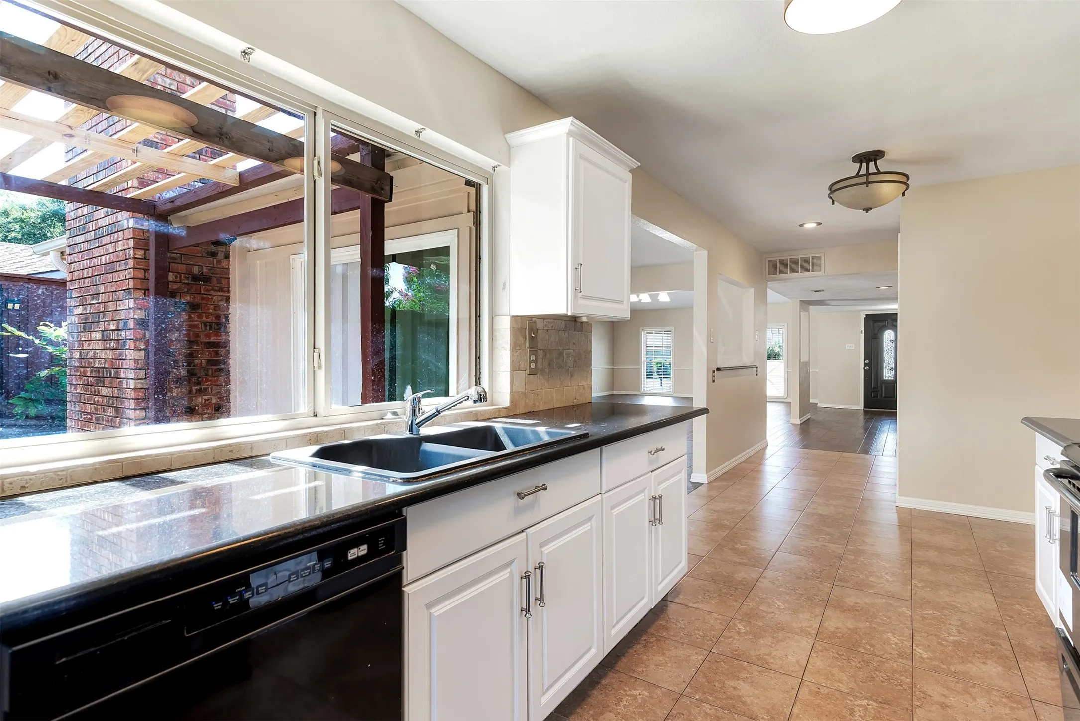Kitchen featuring white cabinetry, dark countertops, a dual basin sink, a built-in dishwasher, and tile flooring