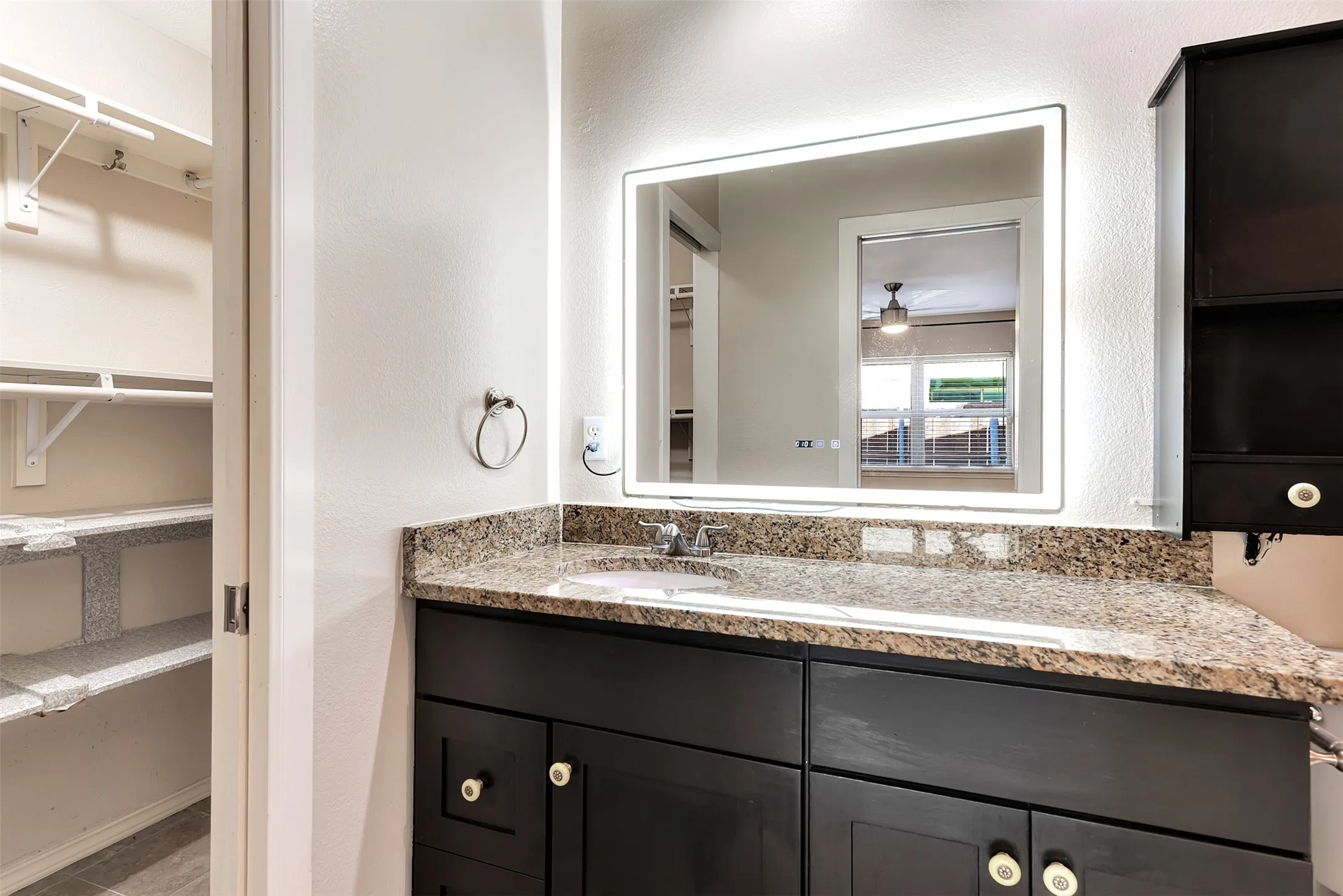 Bathroom vanity with a granite countertop, integrated sink, and modern illuminated mirror