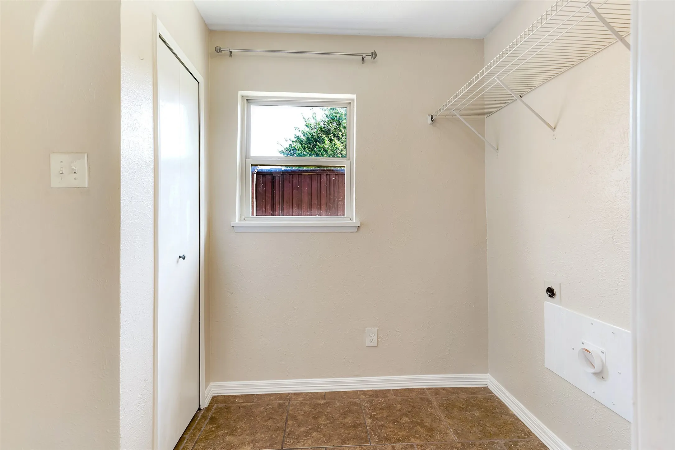 Tiled flooring, white trim, single window, wire shelving, and a bi-fold door