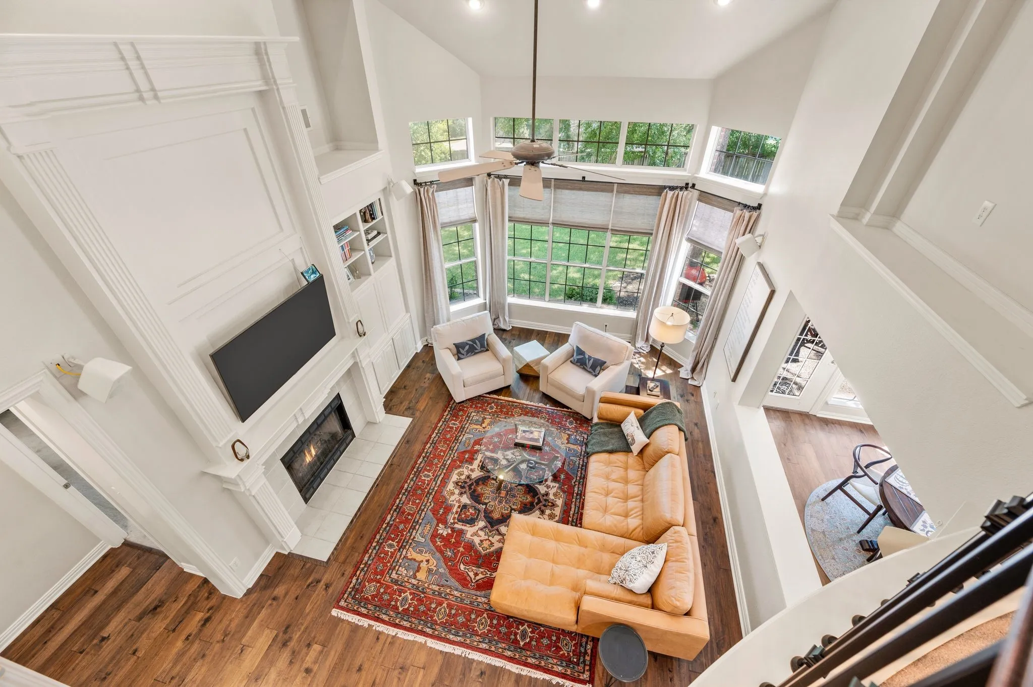View from the upstairs landing showcases the light-filled family room, towering windows, fireplace & built-in cabinetry below.