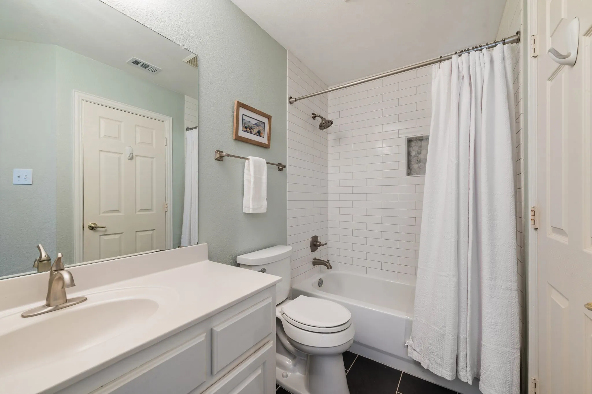 Updated full bath offers a clean, timeless look with white subway tile, a built-in shower niche & dark tile flooring.