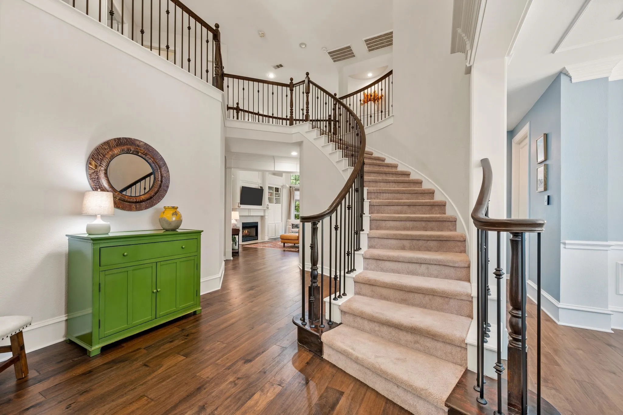 The graceful curved staircase creates a striking centerpiece beneath the soaring two-story ceiling.