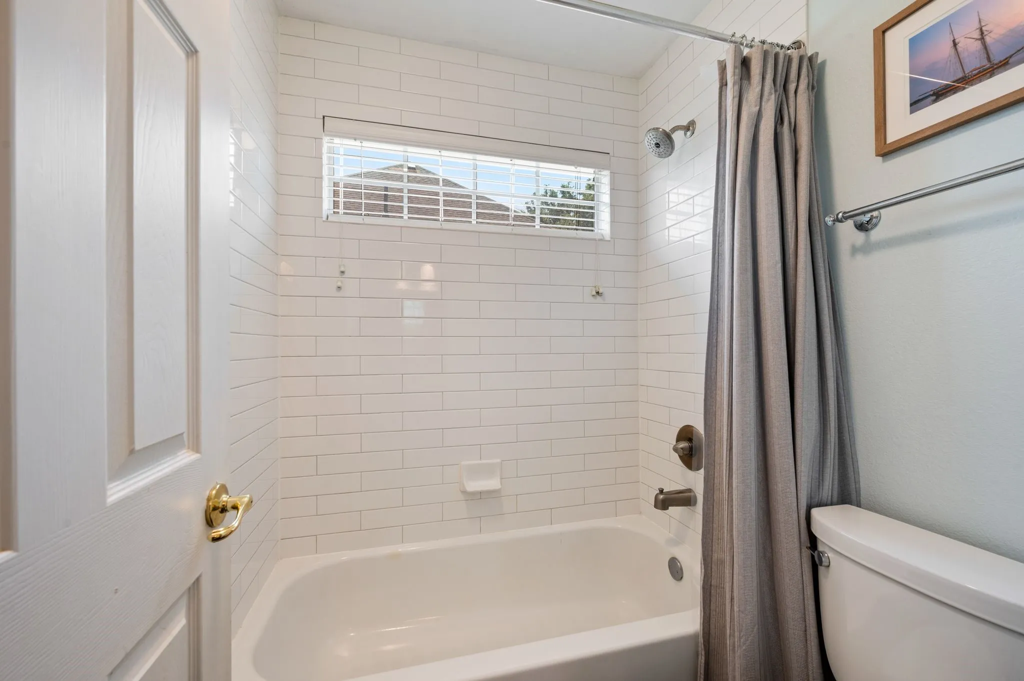 Secondary full bath features a tub-shower combination surrounded by crisp white subway tile & a window for natural light.