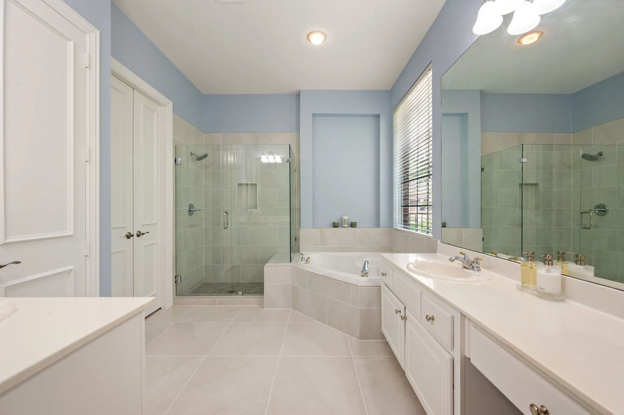 Generous owner’s bath offers separate vanities, a jetted soaking tub, frameless glass shower & abundant natural light.