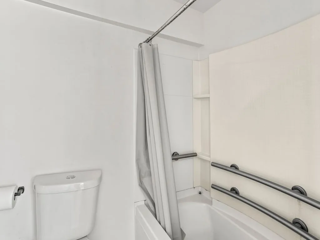 White bathtub with an integrated shower, featuring a built-in shelf and grab bars