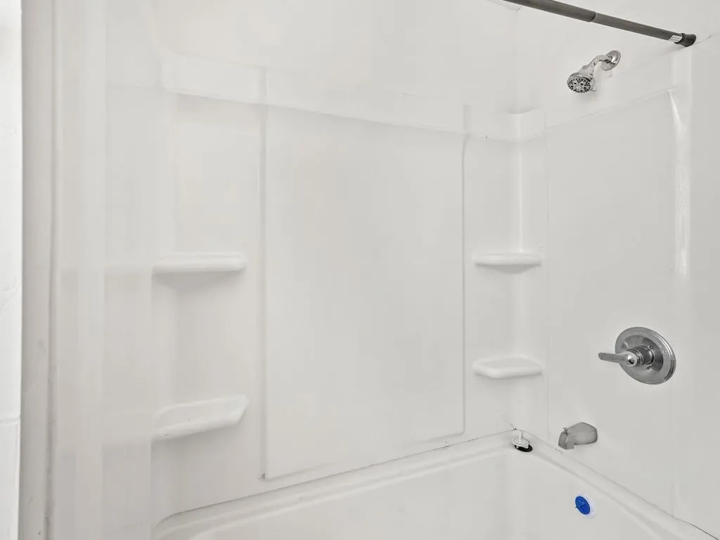 White shower surround with built-in shelving, chrome shower head, and coordinating faucet