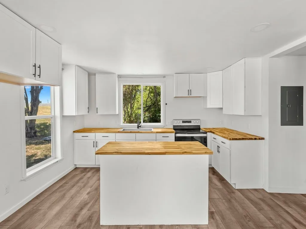 Modern kitchen featuring white cabinetry, wood-finish countertops, stainless steel range, a central island, and wood-finish flooring