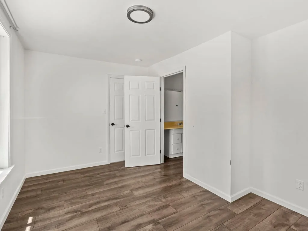 Wood-finish flooring, white walls, white trim, overhead flush-mount lighting, and a window with white casing