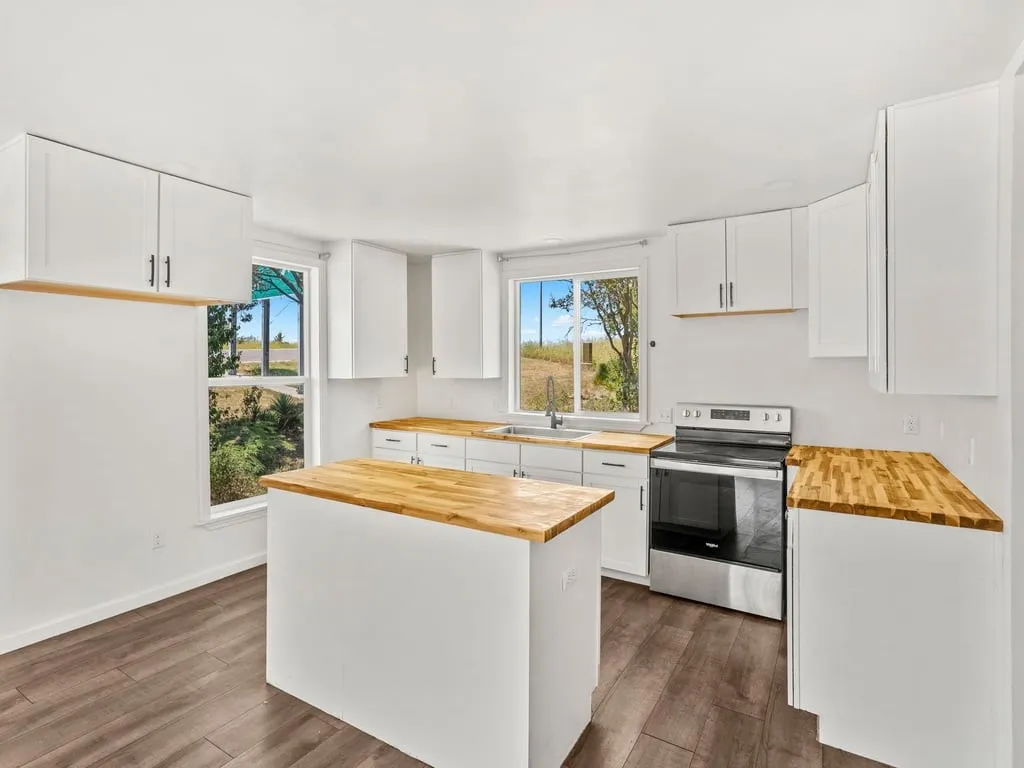 Kitchen featuring wood-finish flooring, white cabinetry, wood countertops, a stainless steel range, and a center island
