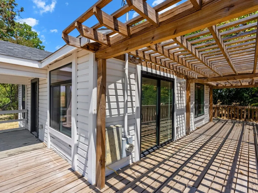 Expansive wood-finish decking with a wooden pergola, multiple sliding glass doors, and white siding