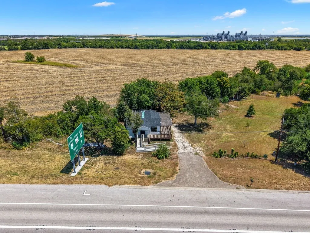 Roadside property with a private driveway, surrounded by mature trees and expansive open fields