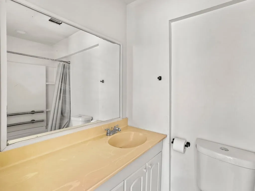 Bathroom with an integrated sink vanity, wall-mounted mirror, and a toilet