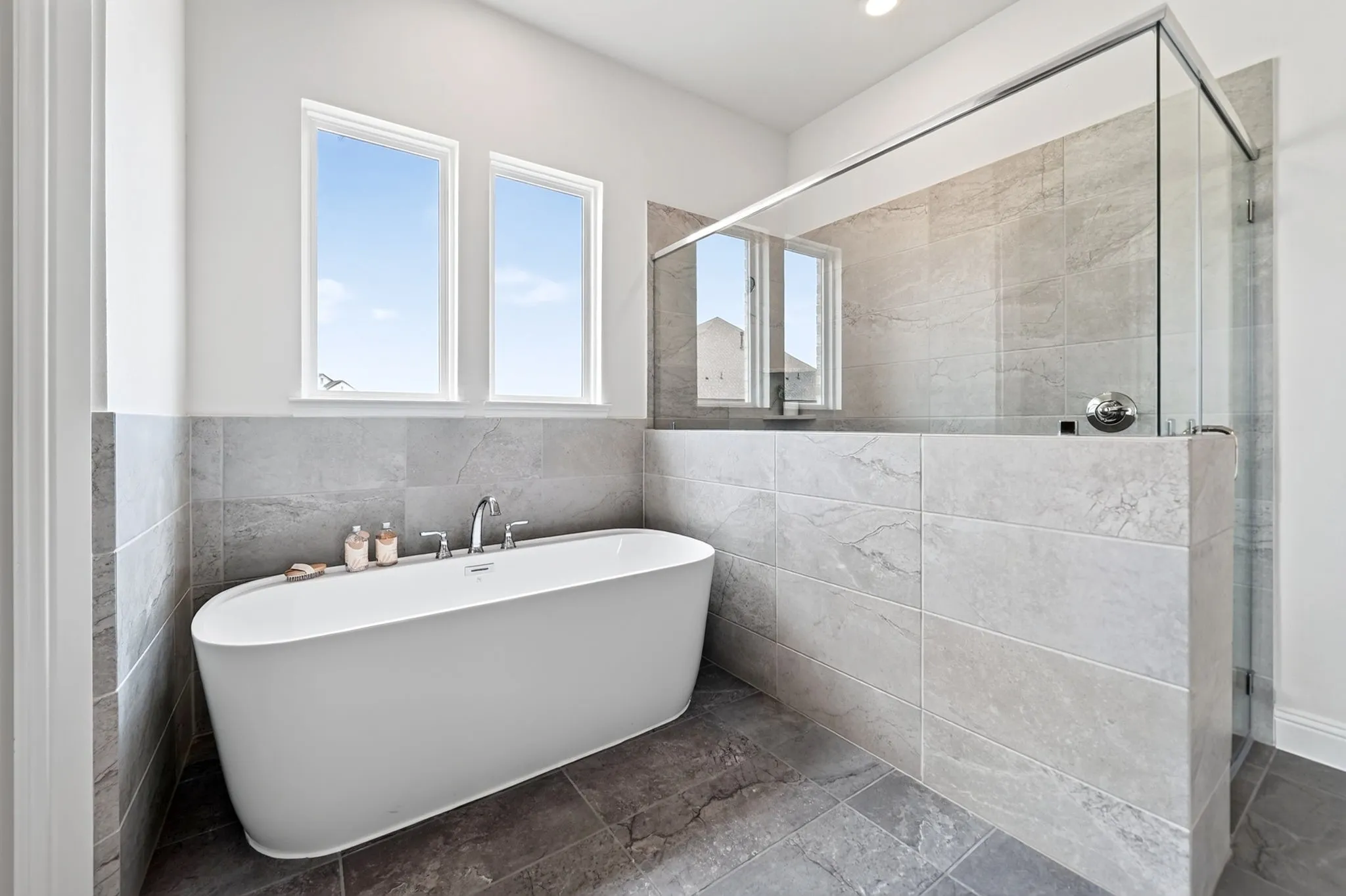 Freestanding soaking tub with chrome fixtures, tiled shower with glass enclosure, dual windows, and recessed lighting