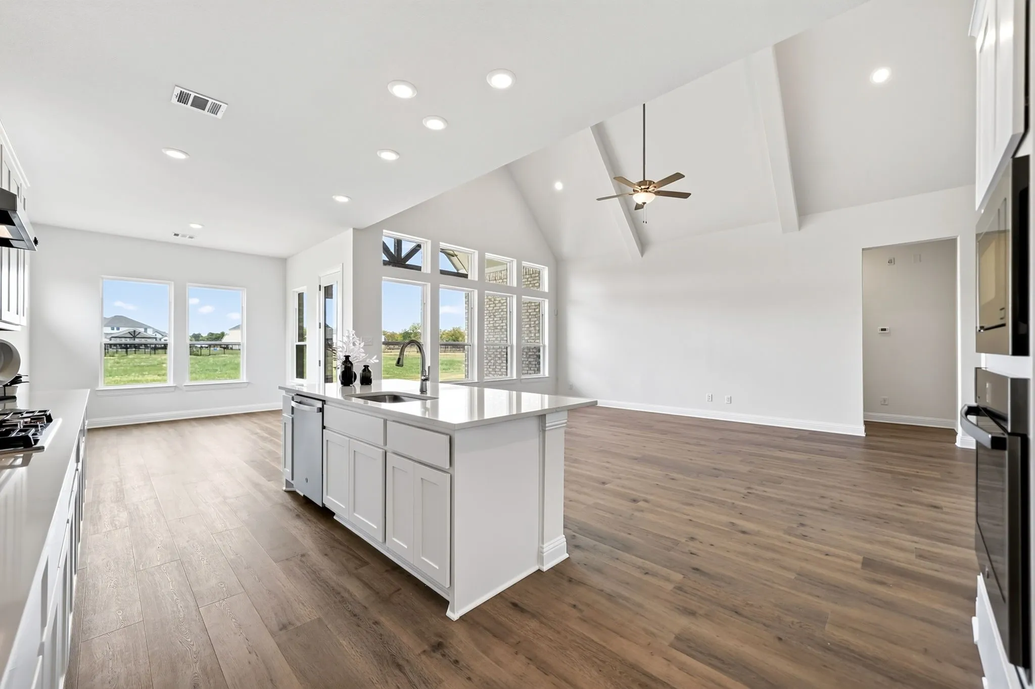 Open concept living area featuring a kitchen island with sink, wood-finish flooring, vaulted ceiling, and recessed lighting