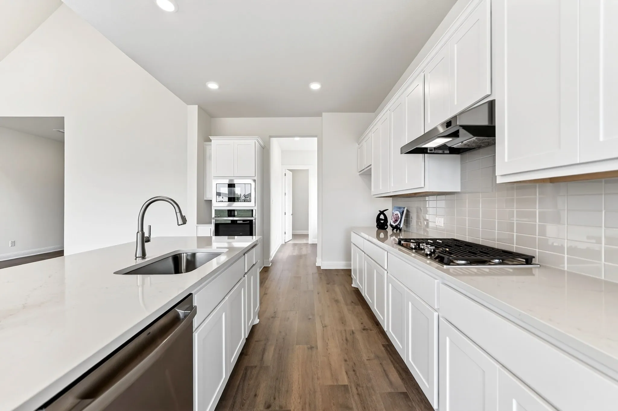 Kitchen featuring wood-finish flooring, white cabinetry, integrated stainless steel appliances, and a gas cooktop