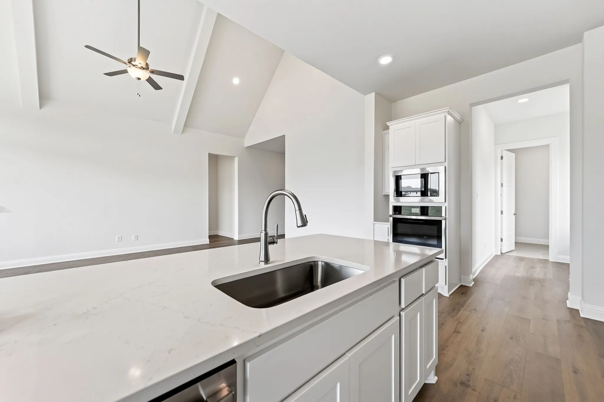 Kitchen island with integrated sink and chrome faucet, built-in microwave and oven, wood-finish flooring, and vaulted ceiling with exposed beams