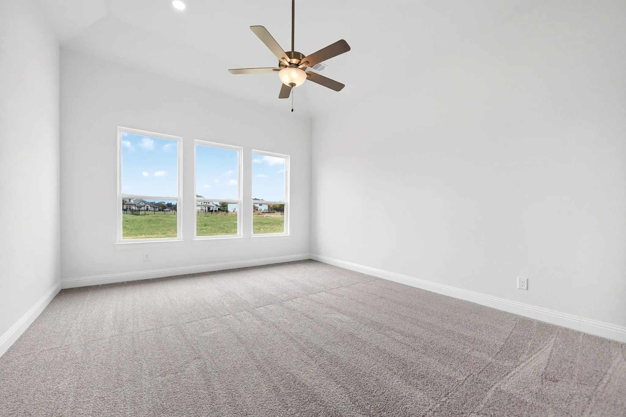 Vaulted ceiling, recessed lighting, ceiling fan with integrated light, three large windows, and carpet flooring