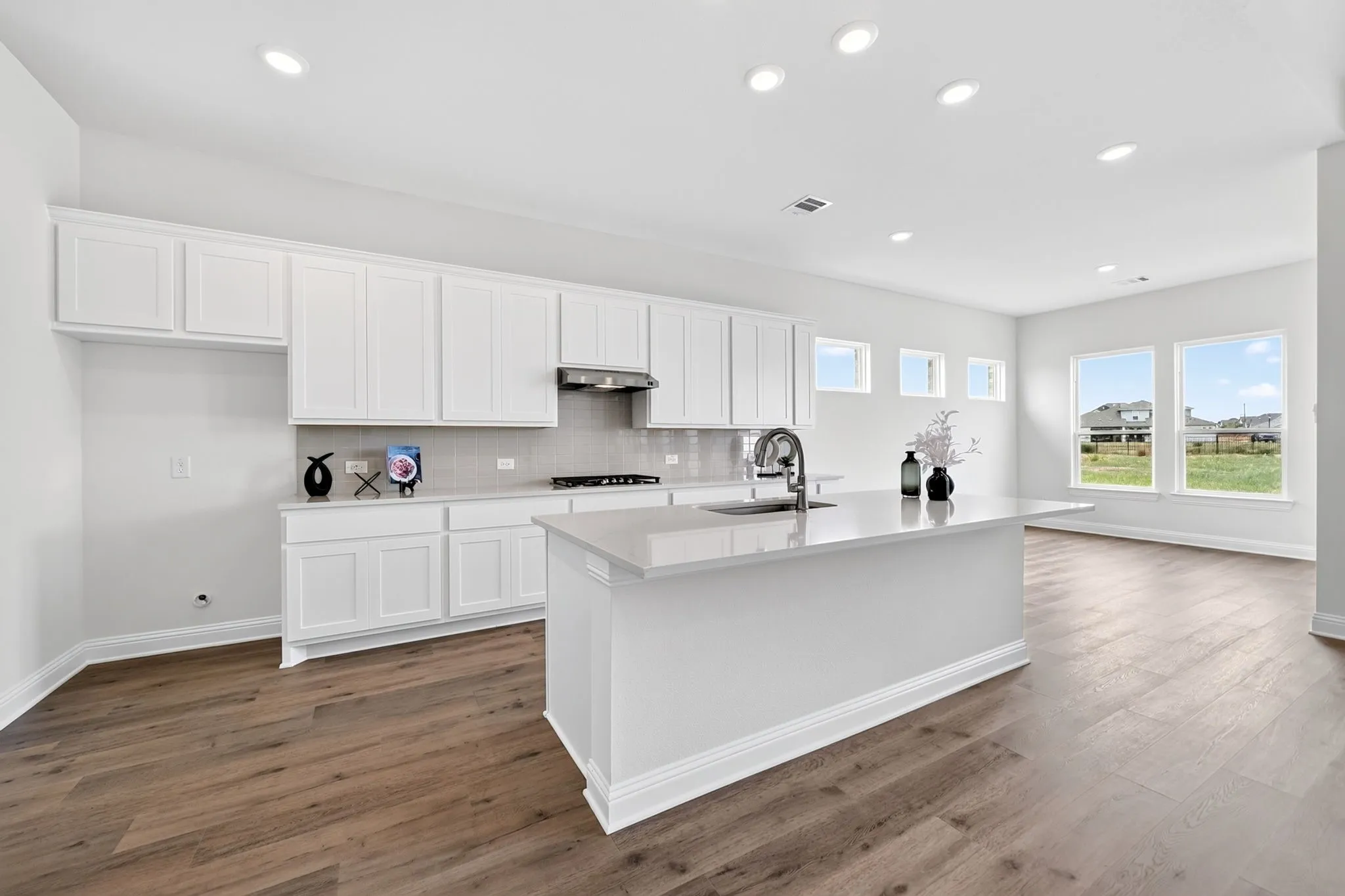 Expansive kitchen featuring white cabinetry, a center island with sink, wood-finish flooring, and ample natural light from multiple windows