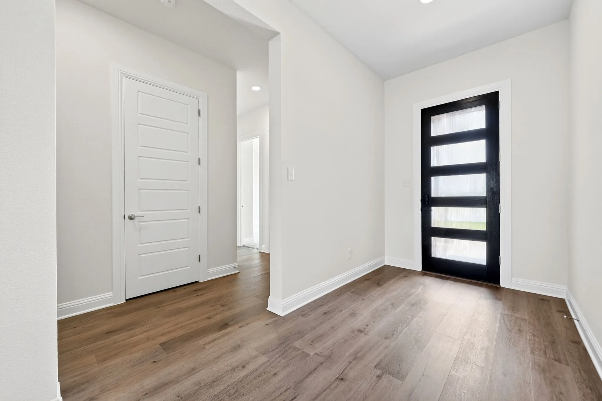 Entryway featuring wood-finish flooring, a modern black door with five frosted glass panels, white interior doors, recessed lighting, and white baseboards