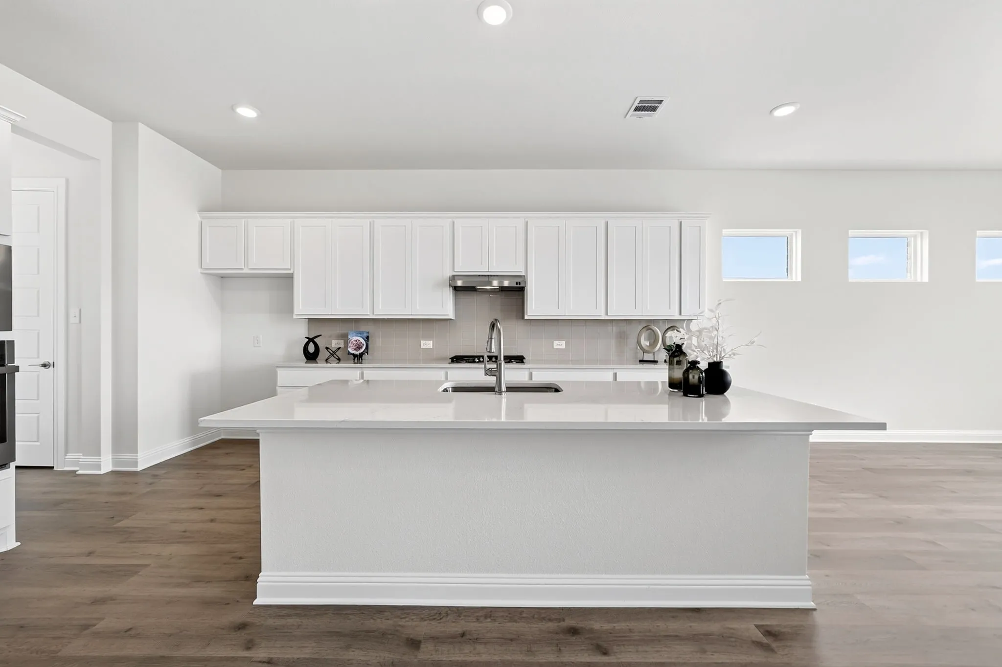 Spacious kitchen featuring an expansive central island, white cabinetry, integrated stainless steel appliances, and wood-finish flooring