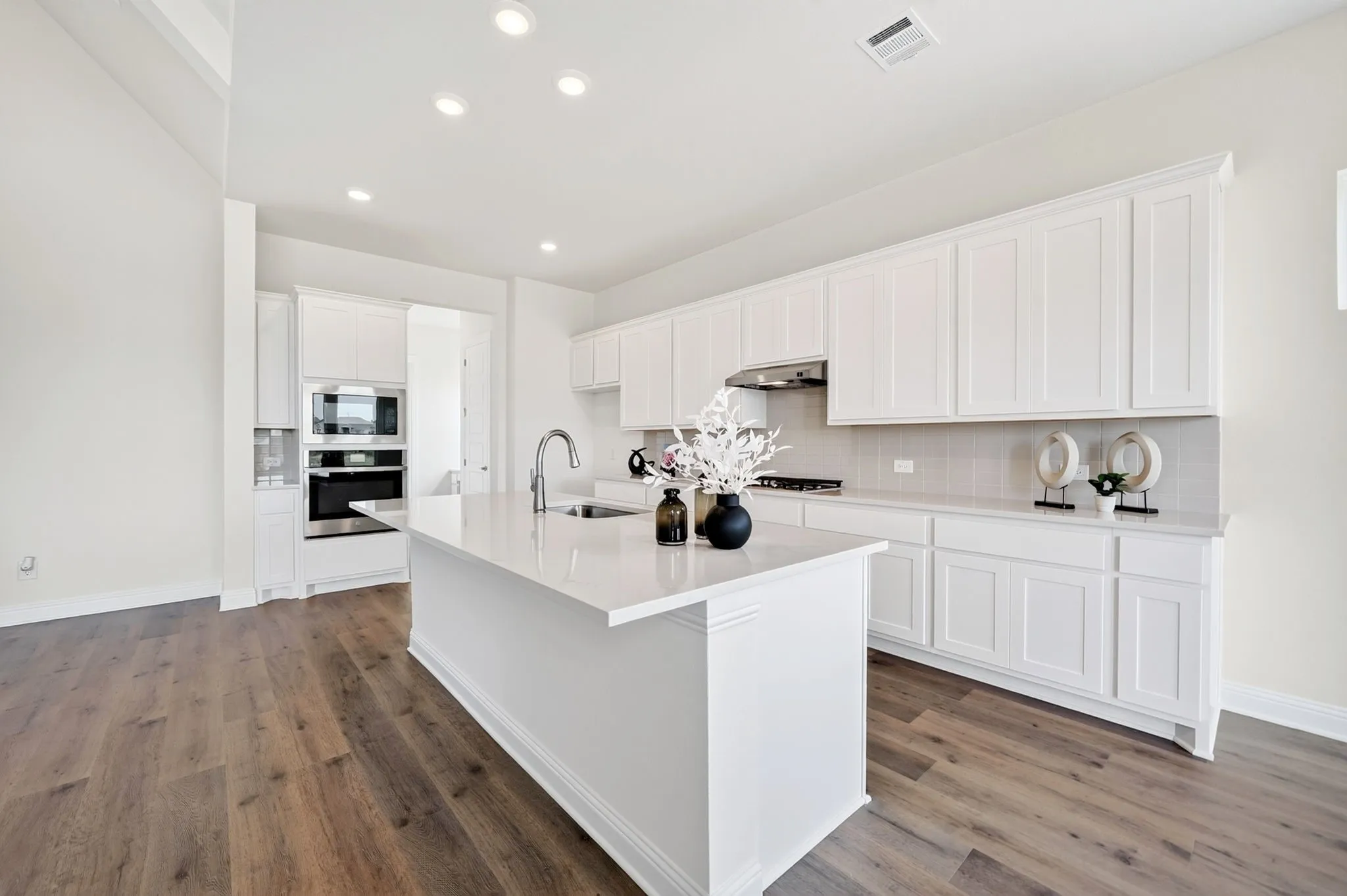 Expansive kitchen featuring wood-finish flooring, recessed lighting, white shaker cabinetry, an integrated stainless steel oven, and a large central island with an undermount sink