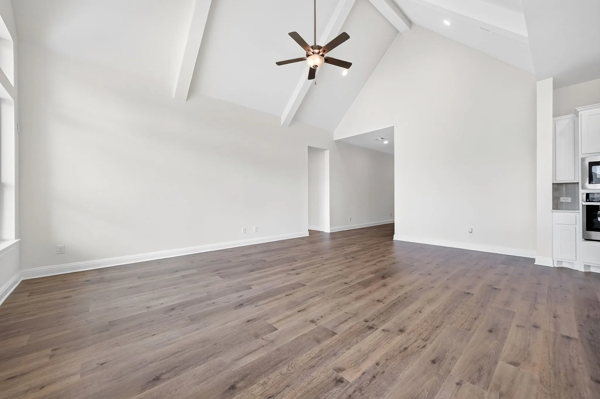 Vaulted ceiling with exposed beams, wood-finish flooring, ceiling fan with integrated lighting, built-in cabinetry, and integrated wall oven