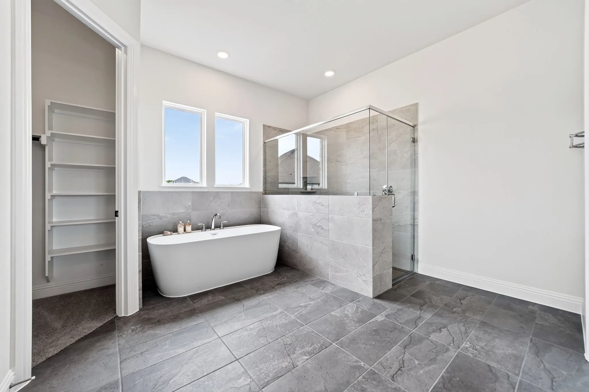 Spacious bathroom featuring a freestanding tub, tiled shower with glass enclosure, large format floor tiling, and a built-in shelving unit