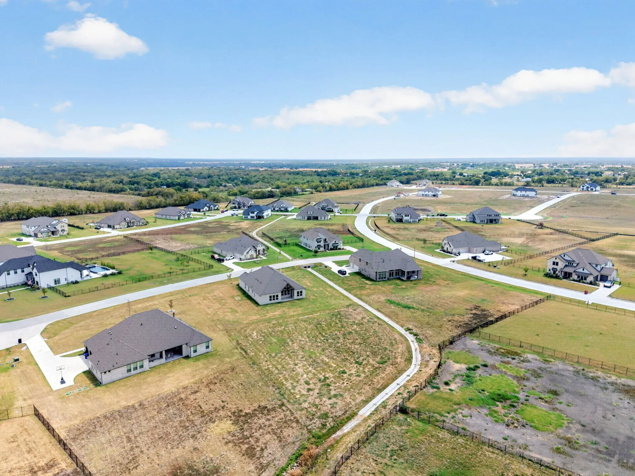 Newly constructed homes with varied architectural styles, asphalt roadways, and expansive undeveloped plots