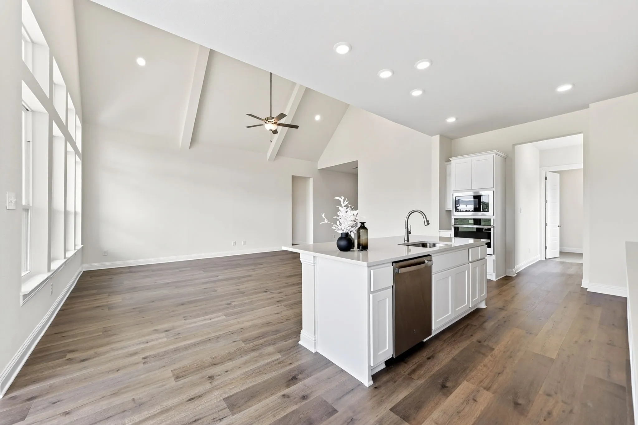 Wood-finish flooring, vaulted ceiling with exposed beams, large multi-pane windows, kitchen island with sink, and built-in stainless steel appliances