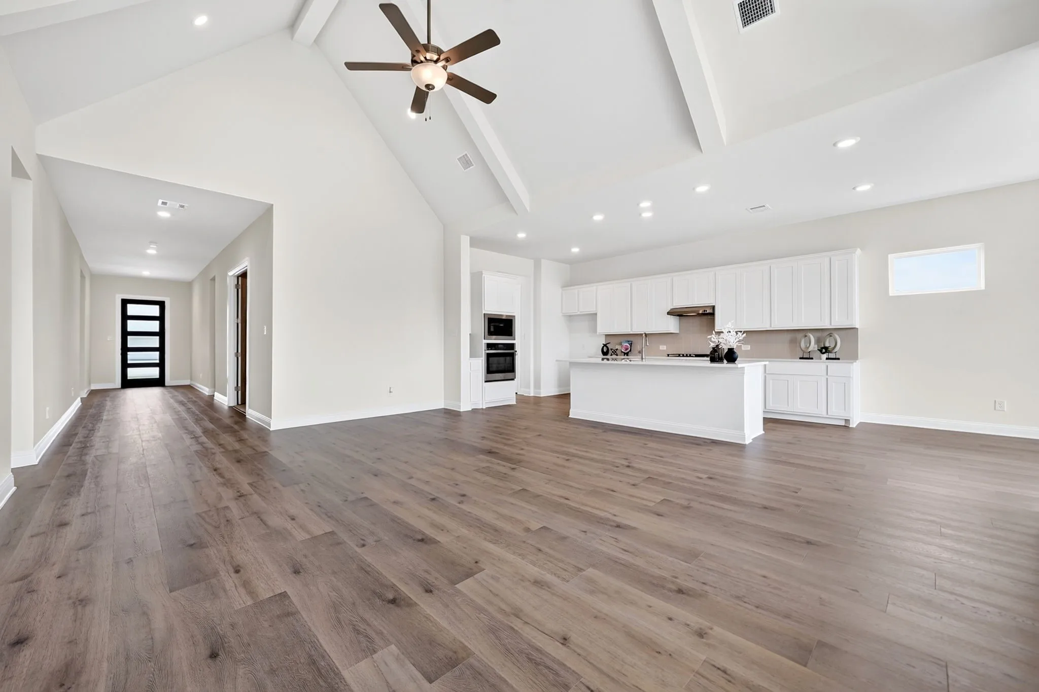 Vaulted ceilings, wood-finish flooring, recessed lighting, ceiling fan, and a kitchen featuring a large island, white cabinetry, and built-in double ovens