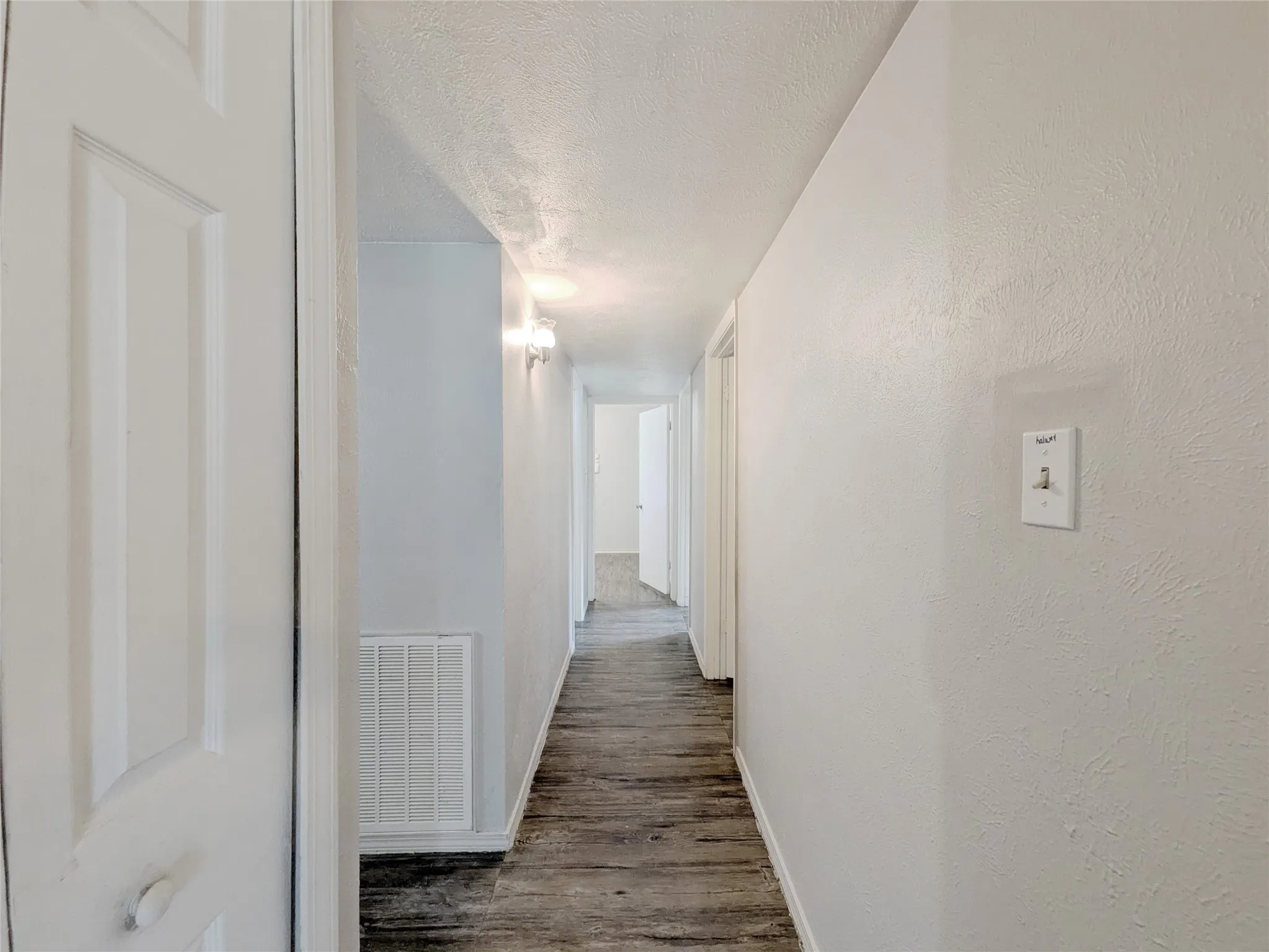 Hallway featuring wood-finish flooring, white painted walls, and wall-mounted light fixtures