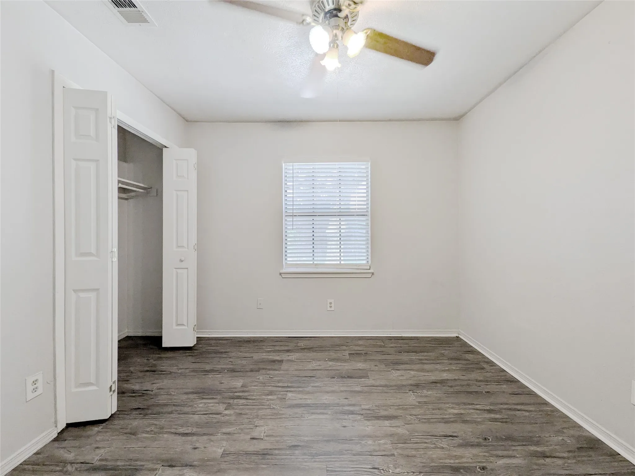 Room featuring wood-finish flooring, a ceiling fan with integrated lighting, a window with blinds, and bi-fold closet doors