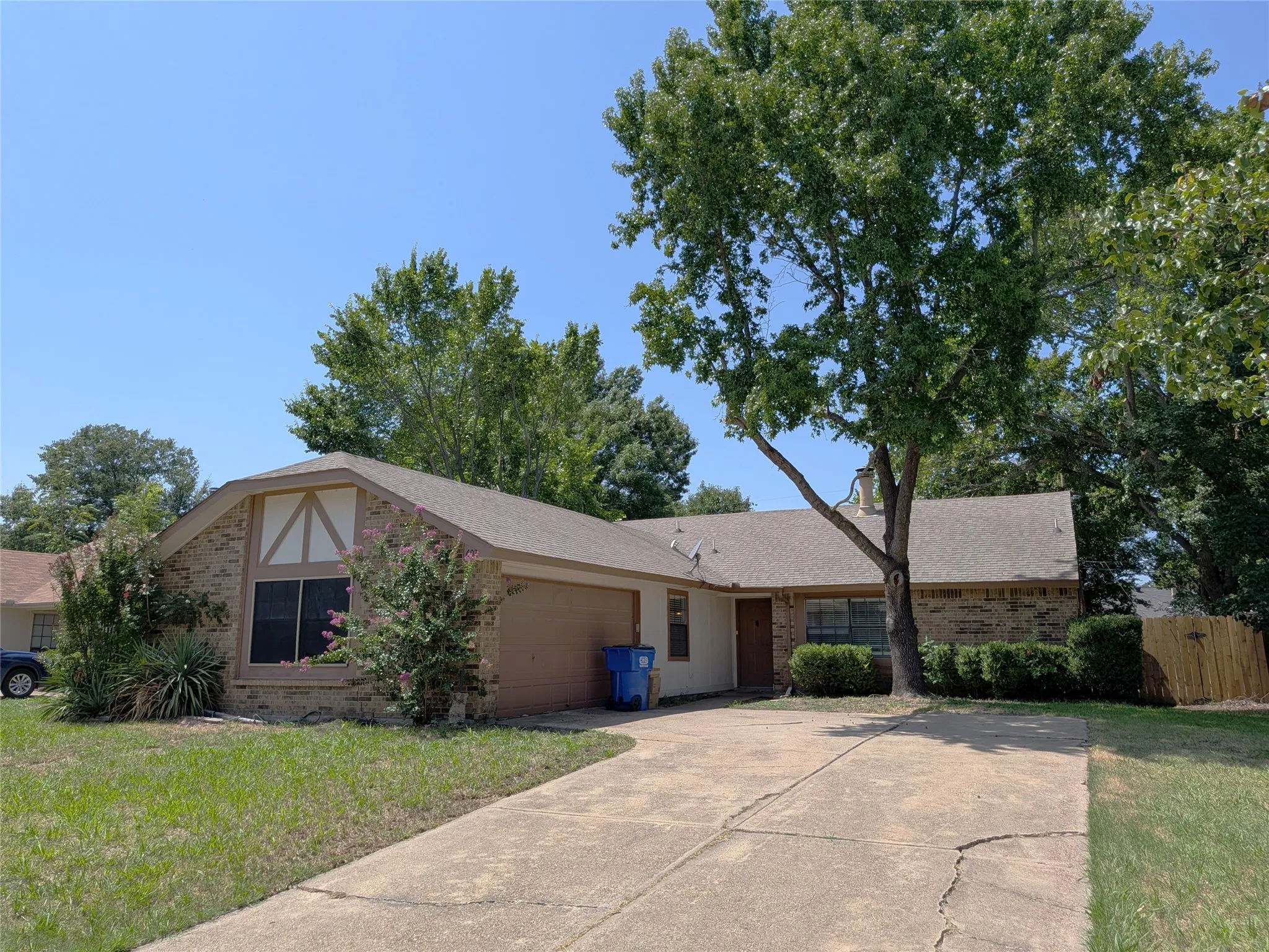 Brick exterior with an attached garage, featuring a gabled roofline and mature tree