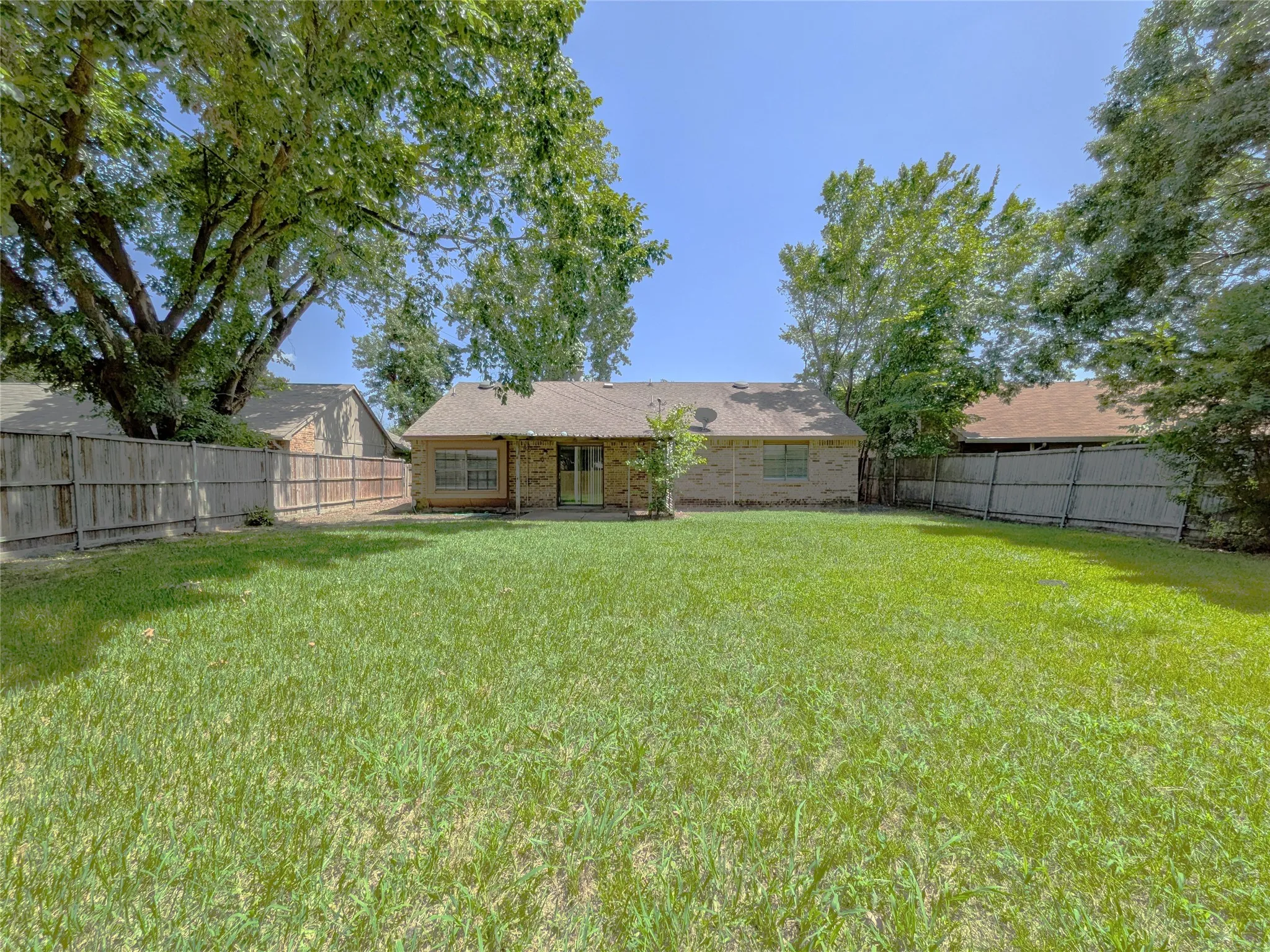 Spacious backyard featuring a large grassy area, privacy fencing, and mature trees
