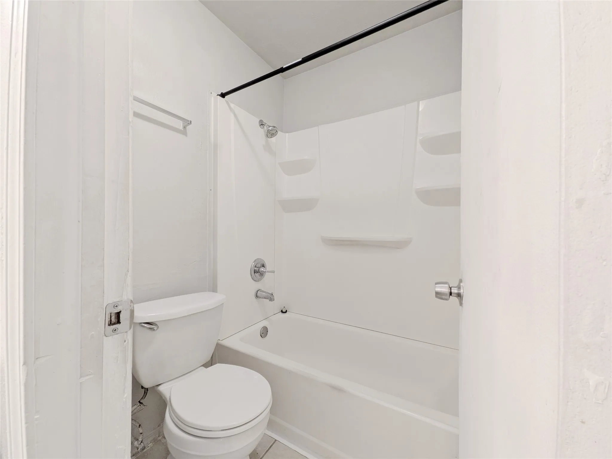 White bathtub with integrated shelving, chrome fixtures, and white toilet
