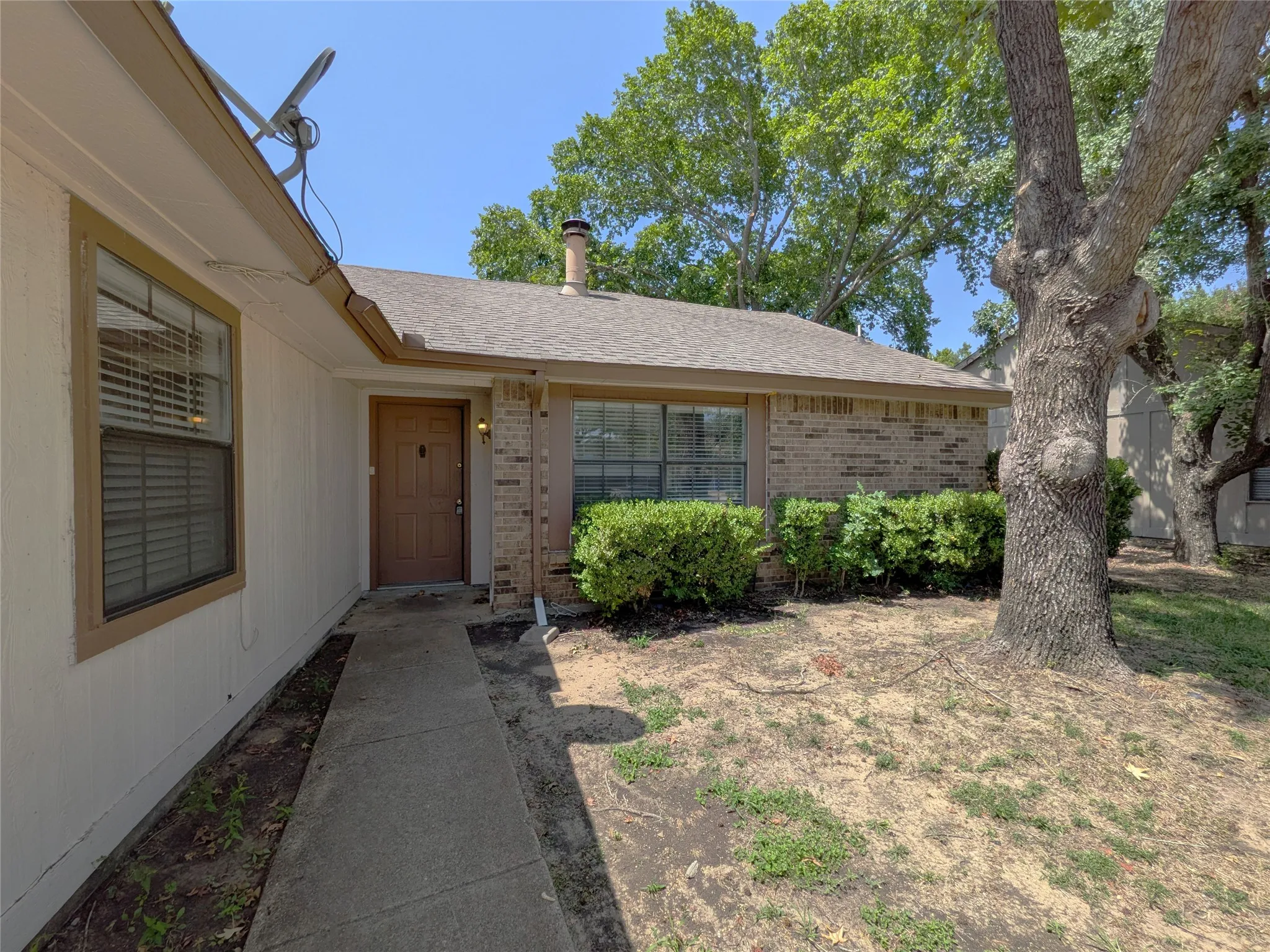 Brick exterior with a prominent front door, mature tree, and established shrubbery