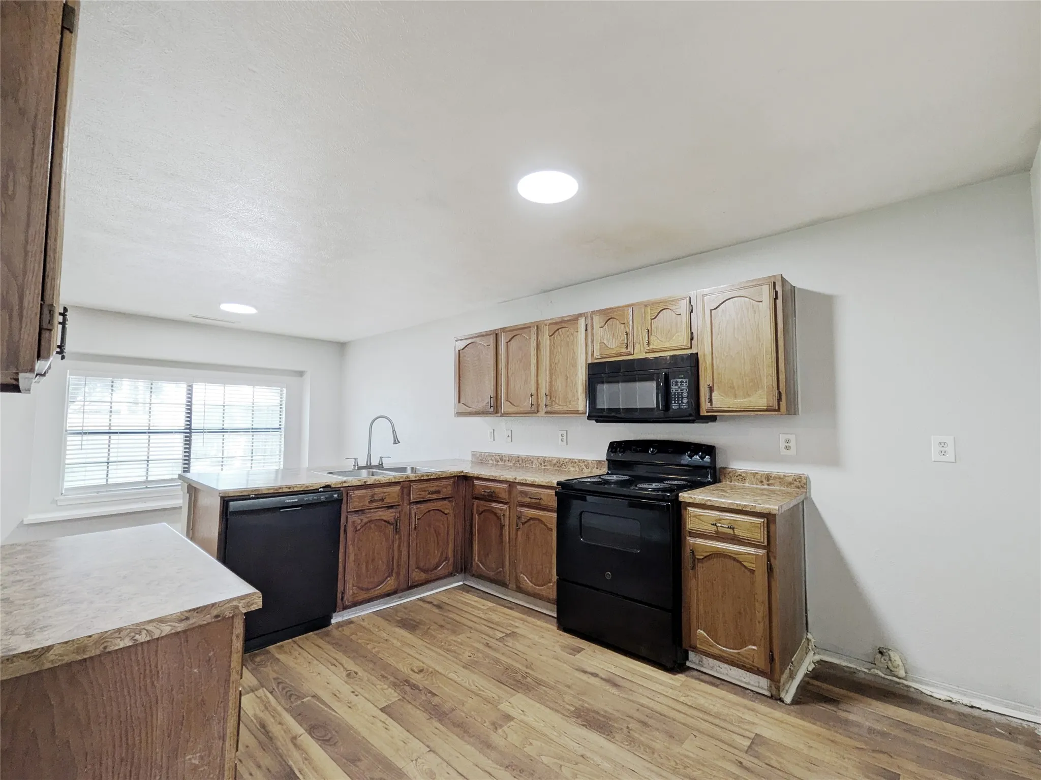Kitchen featuring wood-finish flooring, oak cabinetry, laminate countertops, a stainless steel sink with a gooseneck faucet, and a black appliance suite