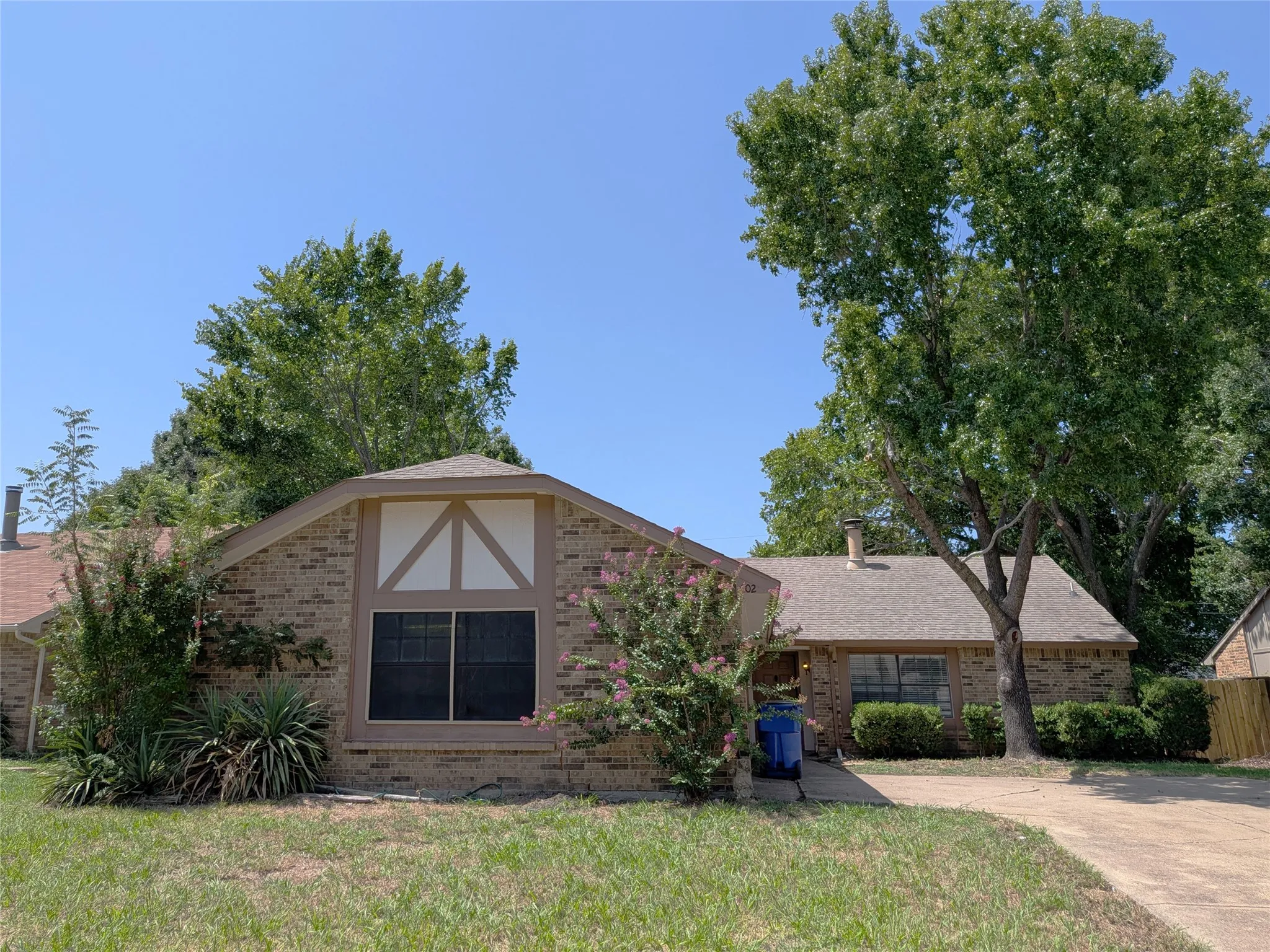 Brick exterior with a gabled roofline, decorative front gable, mature trees, and established landscaping