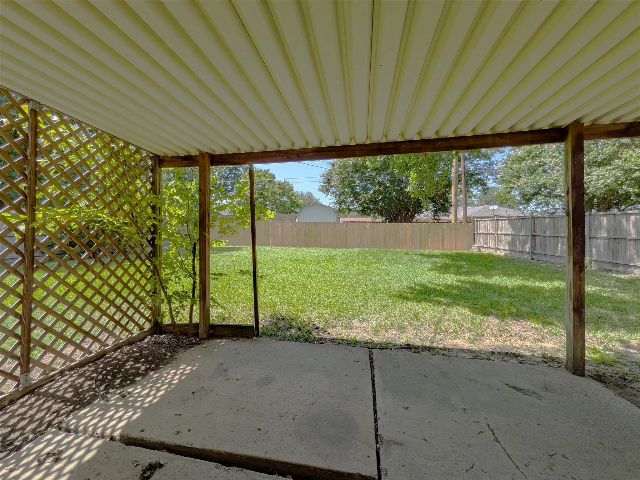 Covered patio with a corrugated metal roof and wooden lattice panel